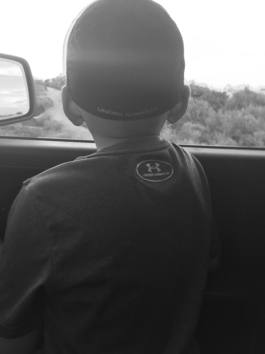 A child wearing a cap looks out from a vehicle.