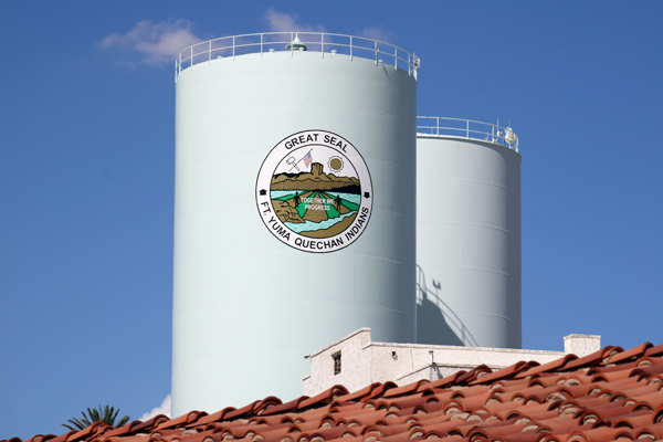 Water tanks displaying the Fort Yuma Quechan Indians seal beneath a blue sky.